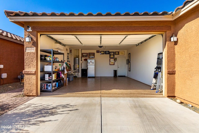 garage with gas water heater, freestanding refrigerator, a wall mounted AC, and concrete driveway