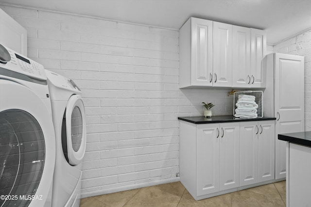 washroom with cabinets, brick wall, light tile patterned floors, and washing machine and dryer