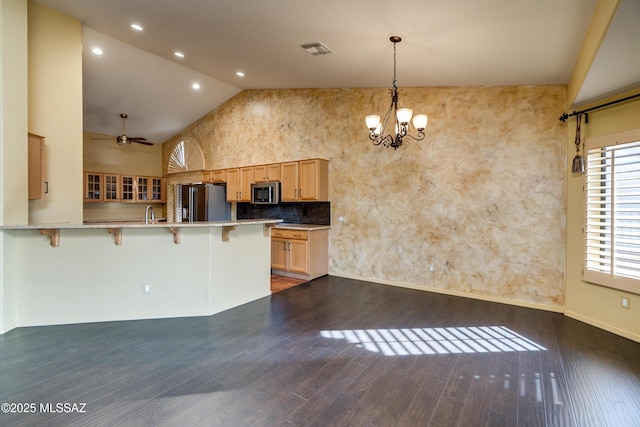 kitchen featuring a breakfast bar area, ceiling fan with notable chandelier, appliances with stainless steel finishes, decorative light fixtures, and kitchen peninsula