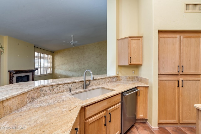 kitchen with sink, light stone counters, stainless steel dishwasher, ceiling fan, and a fireplace