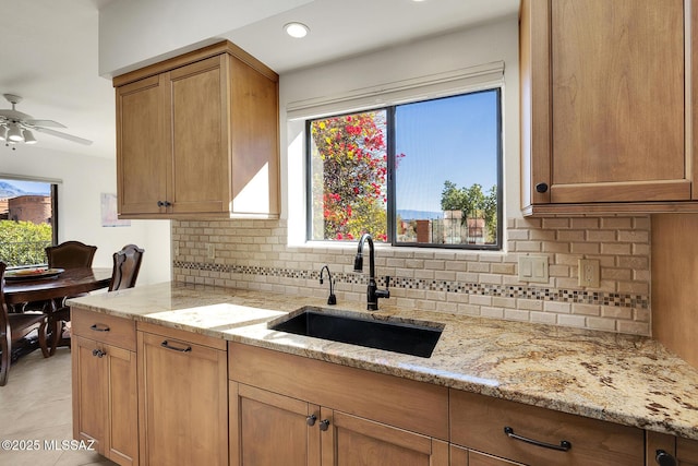 kitchen with light tile patterned flooring, sink, decorative backsplash, ceiling fan, and light stone countertops