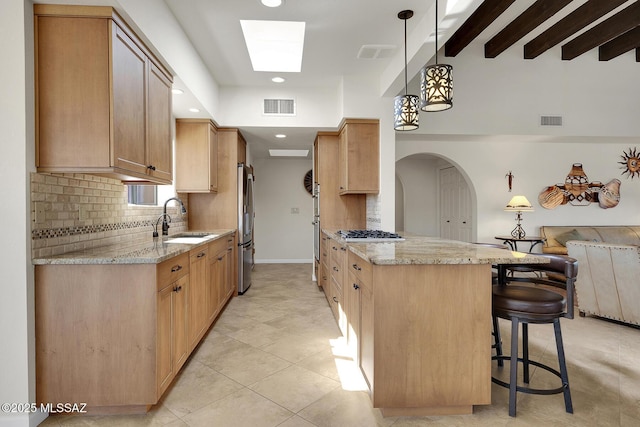 kitchen with stainless steel refrigerator, decorative light fixtures, sink, a kitchen bar, and kitchen peninsula