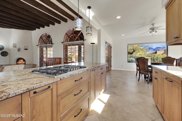 kitchen featuring hanging light fixtures, beamed ceiling, stainless steel gas stovetop, a fireplace, and light stone countertops