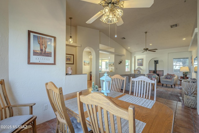 dining space featuring high vaulted ceiling, a wood stove, tile patterned floors, and ceiling fan