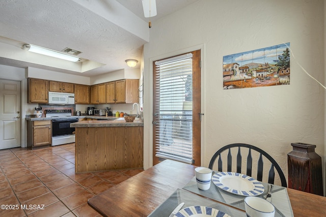 kitchen featuring sink, electric range oven, light tile patterned floors, a textured ceiling, and kitchen peninsula