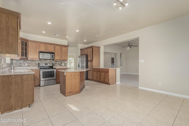 kitchen with sink, light tile patterned floors, a center island, decorative backsplash, and stainless steel appliances