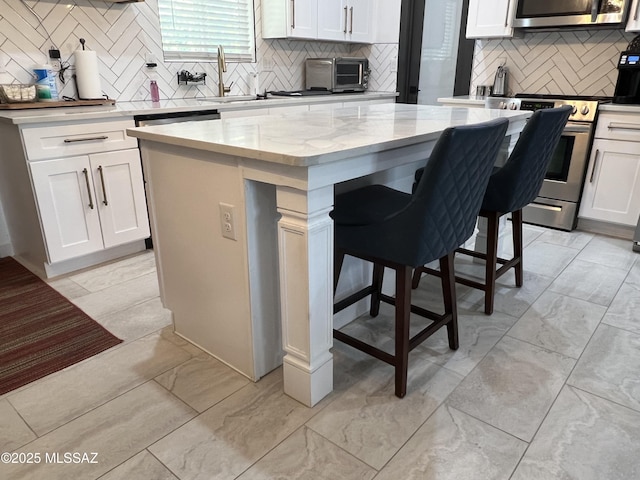 kitchen with a center island, stainless steel stove, white cabinetry, backsplash, and light stone counters