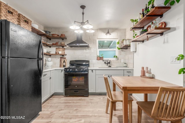 kitchen featuring tasteful backsplash, sink, hanging light fixtures, black appliances, and wall chimney range hood