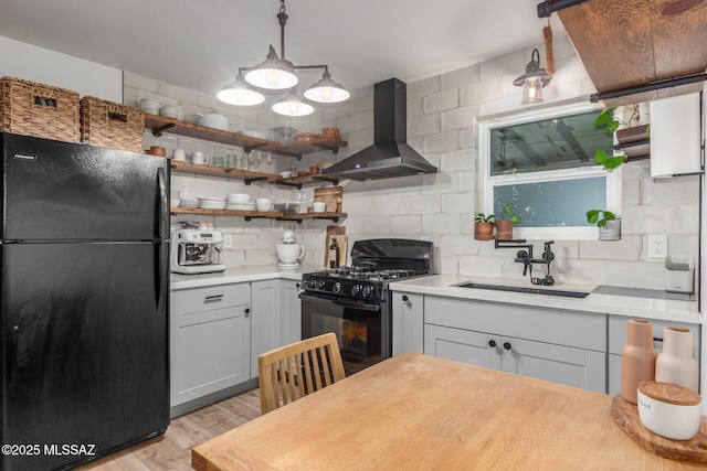 kitchen with gray cabinets, decorative light fixtures, sink, black appliances, and wall chimney exhaust hood