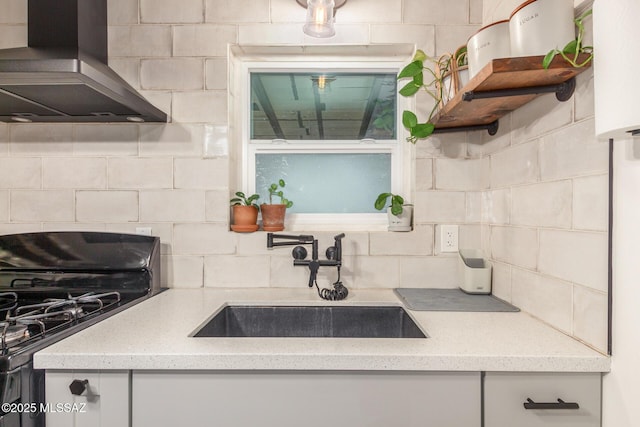 kitchen featuring black gas range oven, sink, range hood, light stone counters, and decorative backsplash