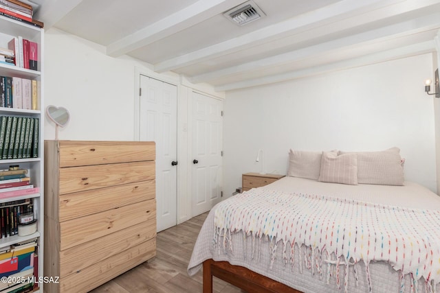 bedroom with wood-type flooring, beam ceiling, and a closet