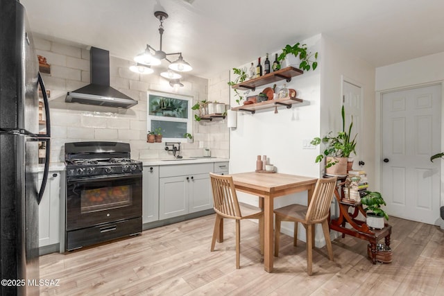 kitchen with wall chimney range hood, sink, backsplash, black appliances, and light wood-type flooring