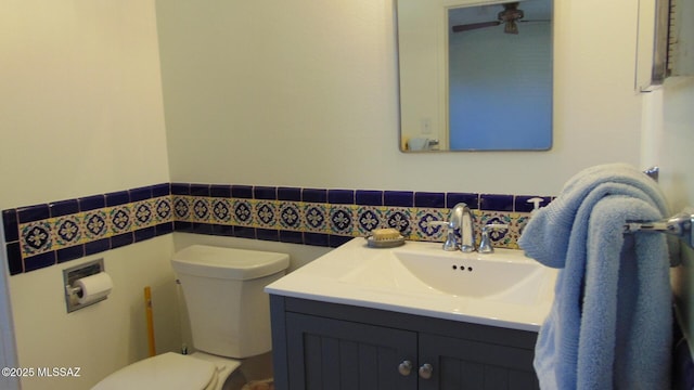 bathroom with ceiling fan, vanity, toilet, and tile walls