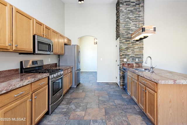 kitchen featuring a high ceiling, light stone countertops, appliances with stainless steel finishes, and sink