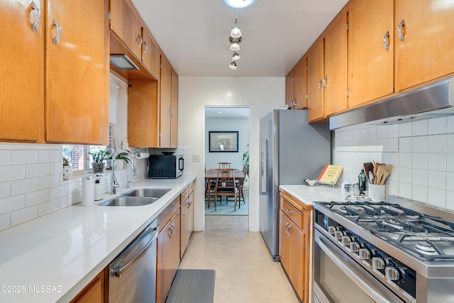 kitchen featuring brown cabinetry, stainless steel appliances, a sink, light countertops, and under cabinet range hood