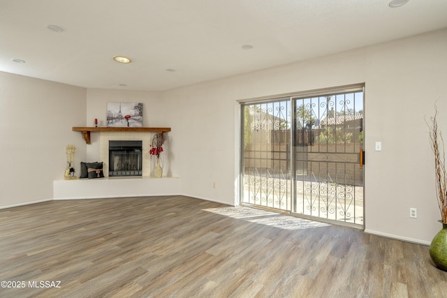 unfurnished living room featuring a tiled fireplace, recessed lighting, wood finished floors, and baseboards