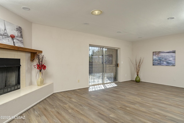 unfurnished living room with a fireplace with raised hearth, baseboards, and wood finished floors