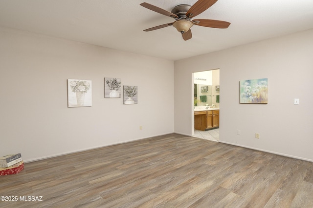 spare room featuring light wood finished floors, baseboards, a ceiling fan, and a sink