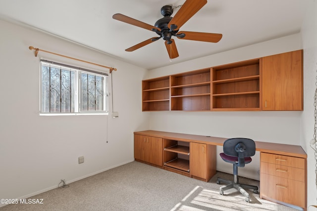 unfurnished office with built in desk, light colored carpet, and ceiling fan