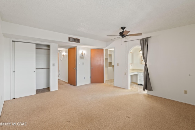 unfurnished bedroom featuring light carpet, connected bathroom, a textured ceiling, and ceiling fan