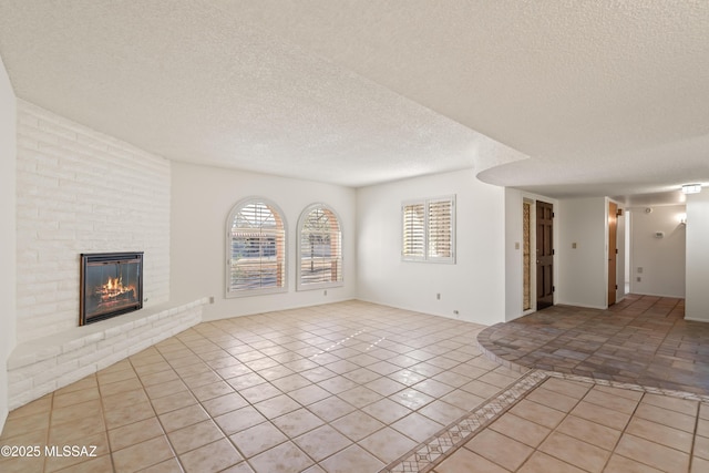 unfurnished living room featuring a brick fireplace, a textured ceiling, and light tile patterned floors