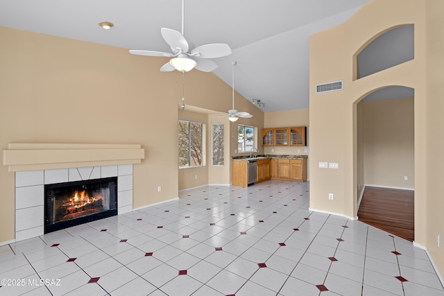 unfurnished living room featuring ceiling fan, light tile patterned floors, sink, a tiled fireplace, and vaulted ceiling