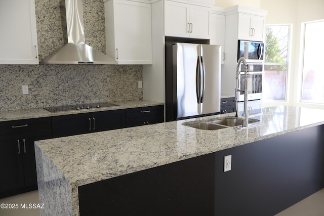 kitchen with appliances with stainless steel finishes, a kitchen island with sink, white cabinets, and wall chimney exhaust hood