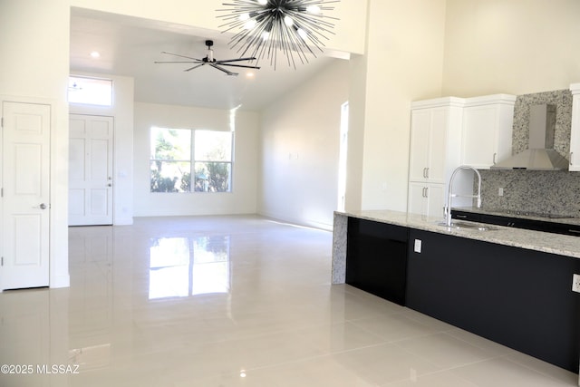 kitchen with a sink, white cabinetry, open floor plan, light stone countertops, and wall chimney exhaust hood