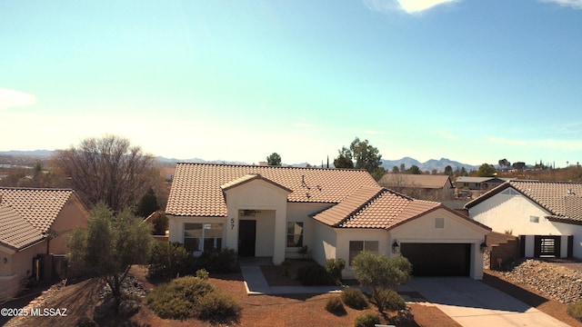 mediterranean / spanish-style home with an attached garage, a mountain view, a tile roof, concrete driveway, and stucco siding