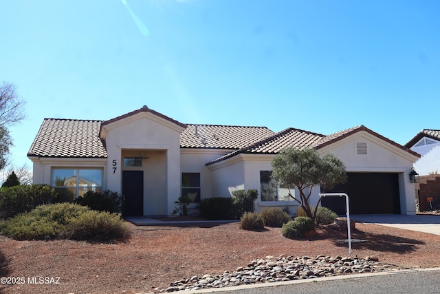 mediterranean / spanish house featuring concrete driveway, an attached garage, a tile roof, and stucco siding