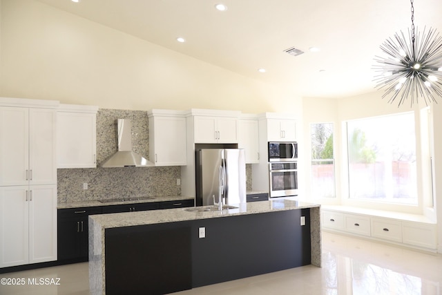 kitchen with appliances with stainless steel finishes, a kitchen island with sink, wall chimney range hood, and white cabinetry