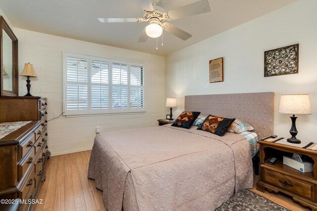 bedroom with ceiling fan, brick wall, and light hardwood / wood-style flooring