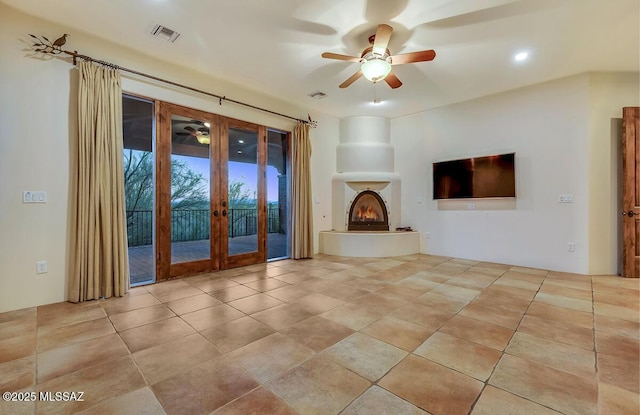 unfurnished living room featuring french doors, a ceiling fan, a warm lit fireplace, and tile patterned floors