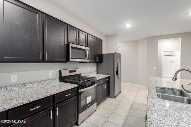 kitchen featuring dark brown cabinetry, sink, light stone counters, light tile patterned floors, and appliances with stainless steel finishes