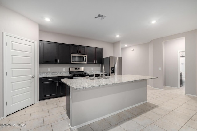 kitchen featuring stainless steel appliances, sink, light stone countertops, and a kitchen island with sink