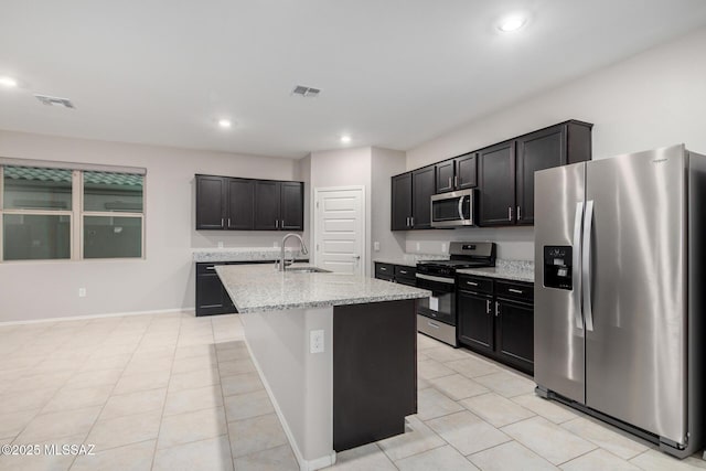 kitchen with sink, a kitchen island with sink, light tile patterned floors, light stone counters, and stainless steel appliances