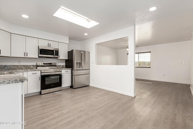 kitchen featuring ceiling fan, a skylight, stainless steel appliances, white cabinets, and light wood-type flooring