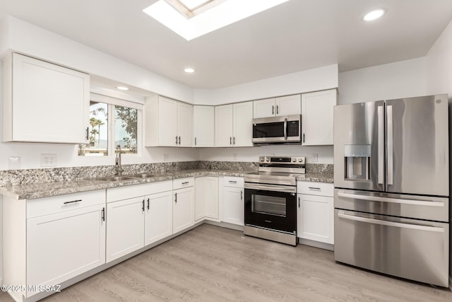 kitchen featuring white cabinetry, stainless steel appliances, a skylight, and sink