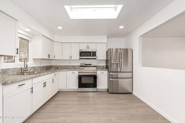 kitchen featuring sink, appliances with stainless steel finishes, a skylight, light stone countertops, and white cabinets