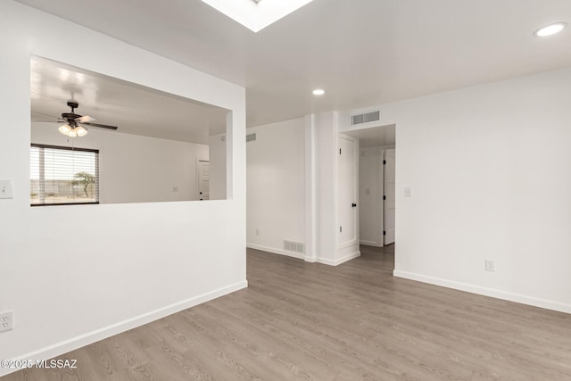 spare room with hardwood / wood-style flooring, ceiling fan, and a skylight