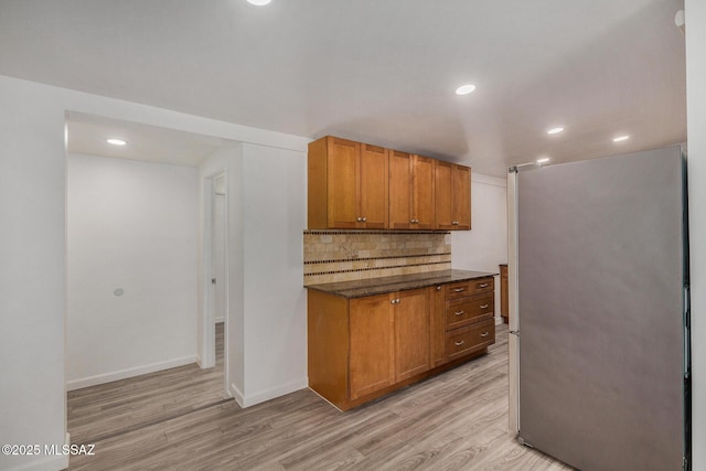 kitchen with tasteful backsplash, dark stone counters, stainless steel refrigerator, and light hardwood / wood-style floors