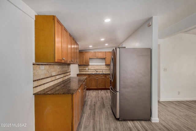 kitchen featuring sink, stainless steel fridge, light hardwood / wood-style flooring, tasteful backsplash, and dark stone counters