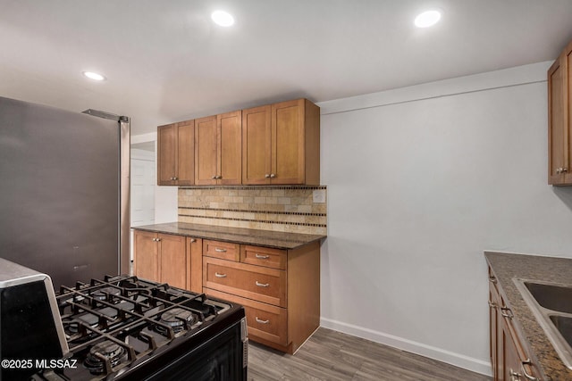 kitchen with tasteful backsplash, dark stone countertops, stainless steel fridge, dark hardwood / wood-style flooring, and black gas stove