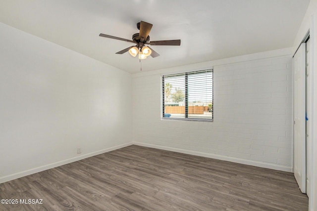 empty room with dark wood-type flooring, ceiling fan, and brick wall