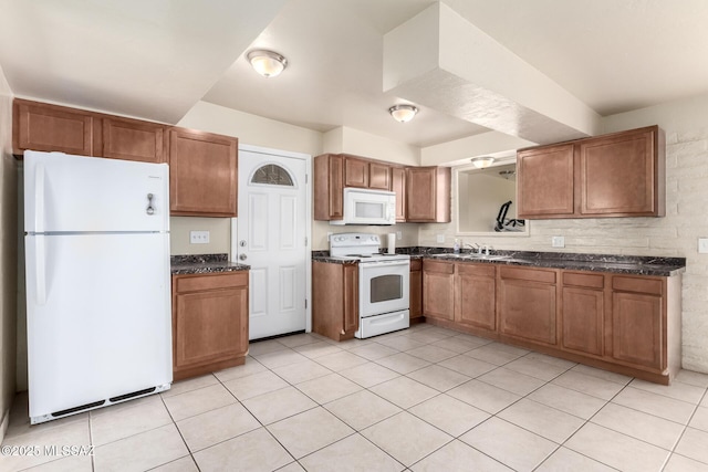 kitchen featuring sink, white appliances, light tile patterned floors, and dark stone countertops