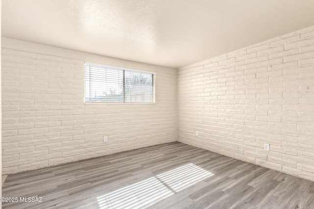 empty room with brick wall and hardwood / wood-style floors