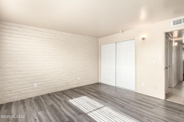 unfurnished bedroom with a closet, brick wall, and dark hardwood / wood-style floors