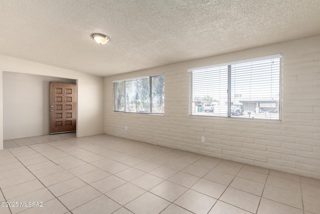 unfurnished room with light tile patterned floors, a textured ceiling, and brick wall