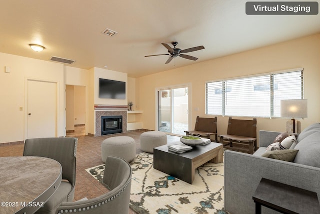 tiled living room with a tile fireplace and ceiling fan