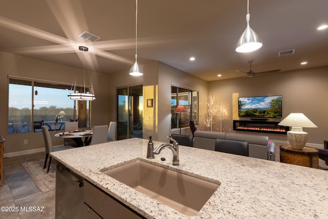 kitchen featuring sink, ceiling fan, black dishwasher, light stone counters, and decorative light fixtures